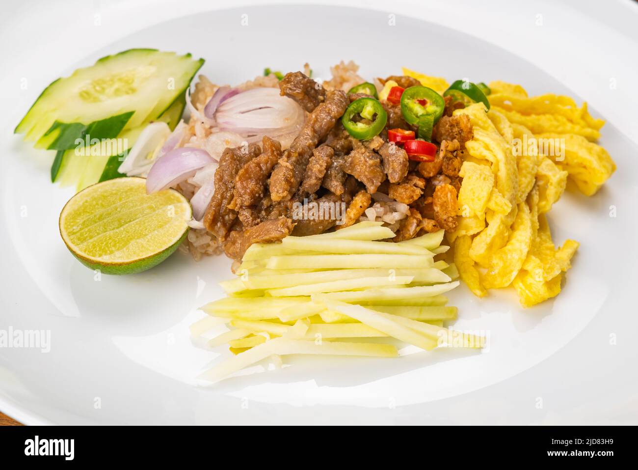 Nahaufnahme von Garnelenpaste gebratenen Reis mit süßem Schweinefleisch, halbe Zitrone, in Scheiben geschnittene Gurken, gehackte frische rohe Mango, geschnittene Zwiebeln, gebratenes Hühnereier und Fre Stockfoto