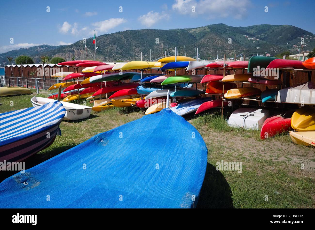 Viele bunte Plastikkajaks liegen auf Lagerregalen vor Bergen am Ufer des Mittelmeers. Kleine Boote im Lager Stockfoto