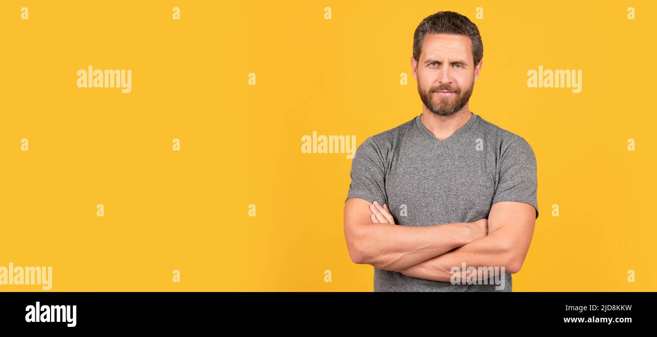 Schöner, reifer muskulöser Mann mit lächelndem Bart auf gelbem Hintergrund gekreuzte Hände, männliche Schönheit. Mann Gesicht Porträt, Banner mit Kopieplatz. Stockfoto