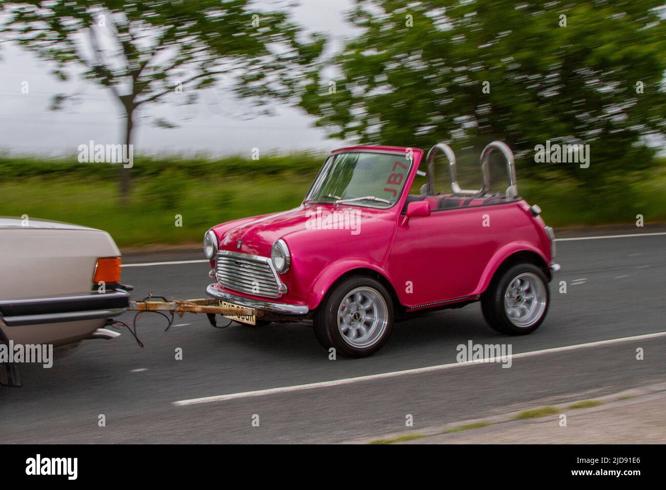1977 70s 70er Jahre pinkfarbenes Leyland Mini 1000 Autos 998cc individuelles verkürztes Fahrzeug wird abgeschleppt by1983 80s Ford Granada; klassischer, moderner Klassiker, Supersportwagen und Spezialfahrzeuge auf dem Weg nach Lytham St Annes, Lancashire, Großbritannien Stockfoto