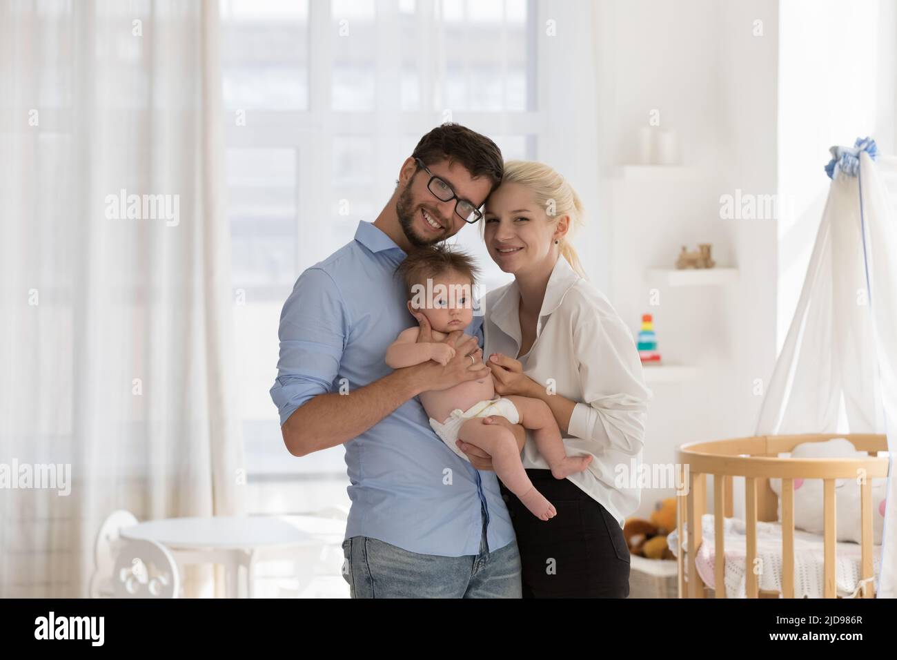 Junge Eltern halten sich an den Armen Baby lächelnd Blick auf die Kamera Stockfoto