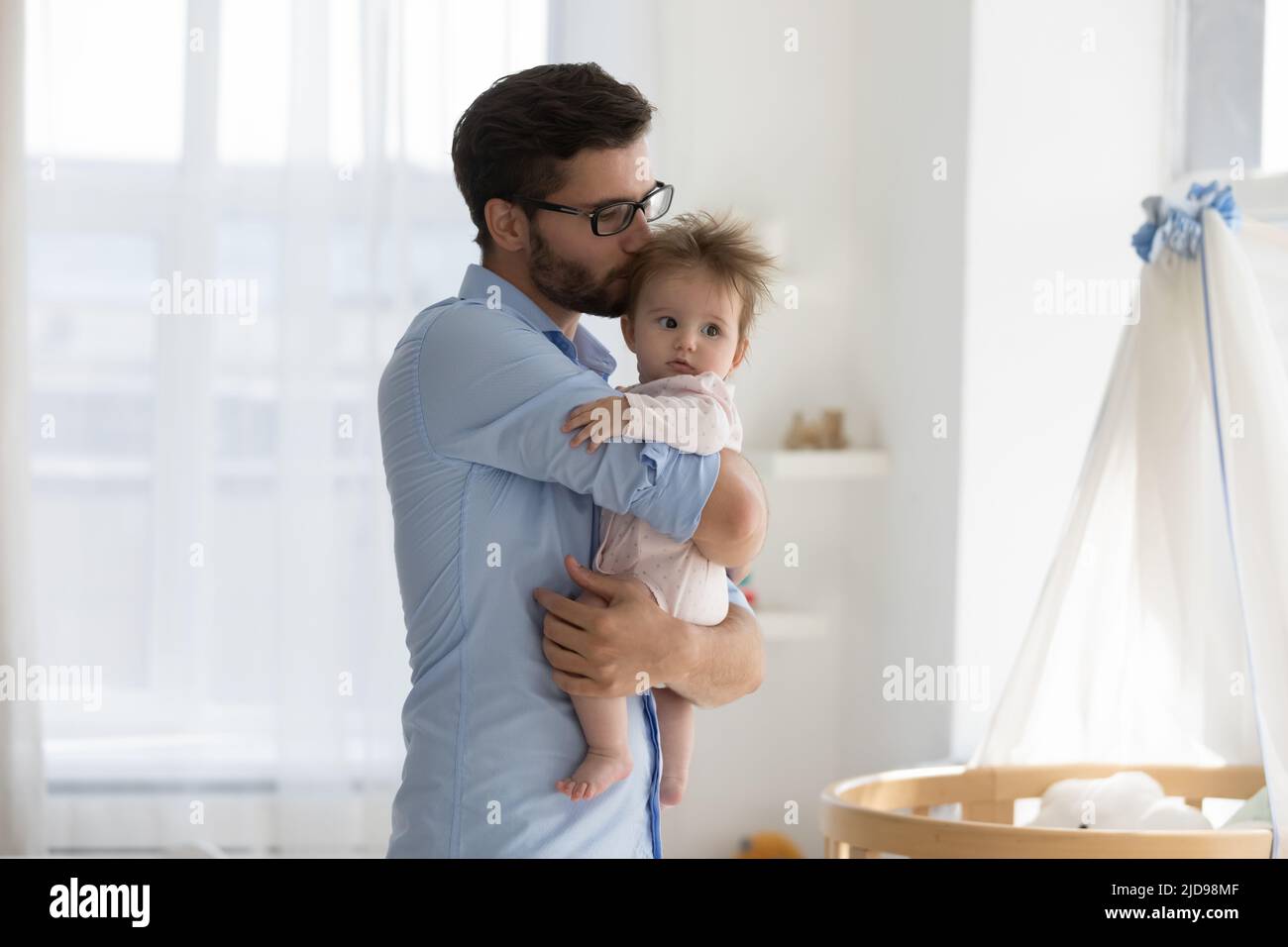 Vita küsst das Baby, das in der Nähe einer modernen Krippe in einer gemütlichen Kinderstube steht Stockfoto