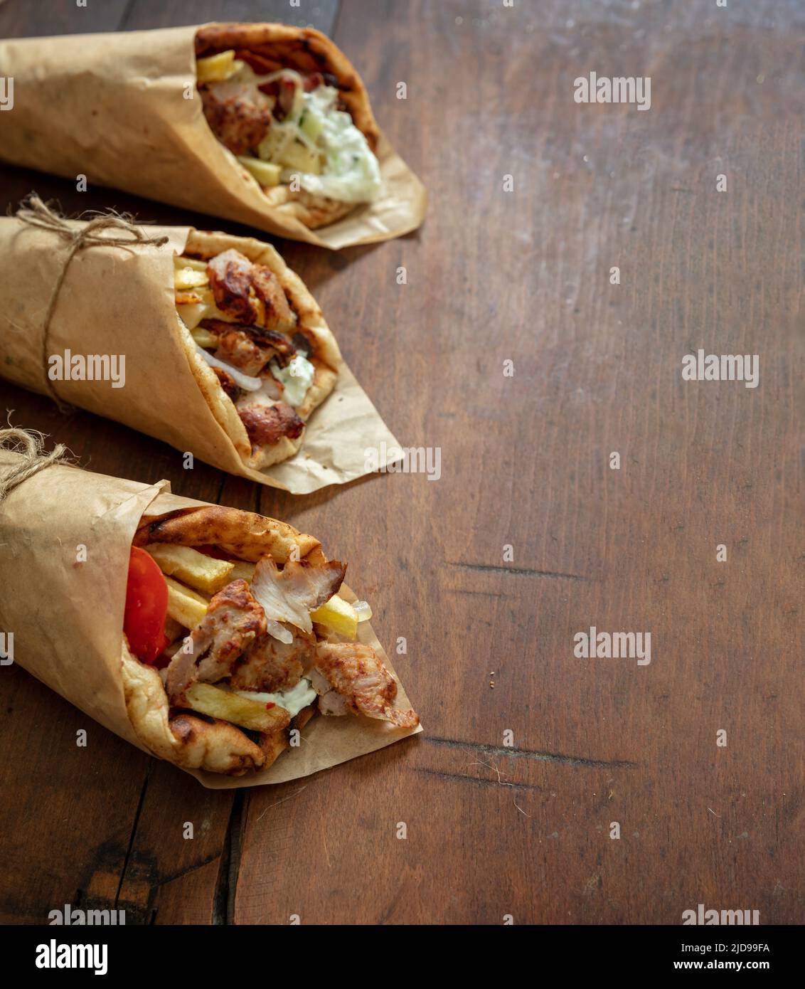 Shawarma Gyro Pita auf Holztisch. Griechische Lebensmittel, Fleisch in Scheiben, Kartoffeln, Tomaten und Zatziki, Papierverpackung, Nahaufnahme. Stockfoto