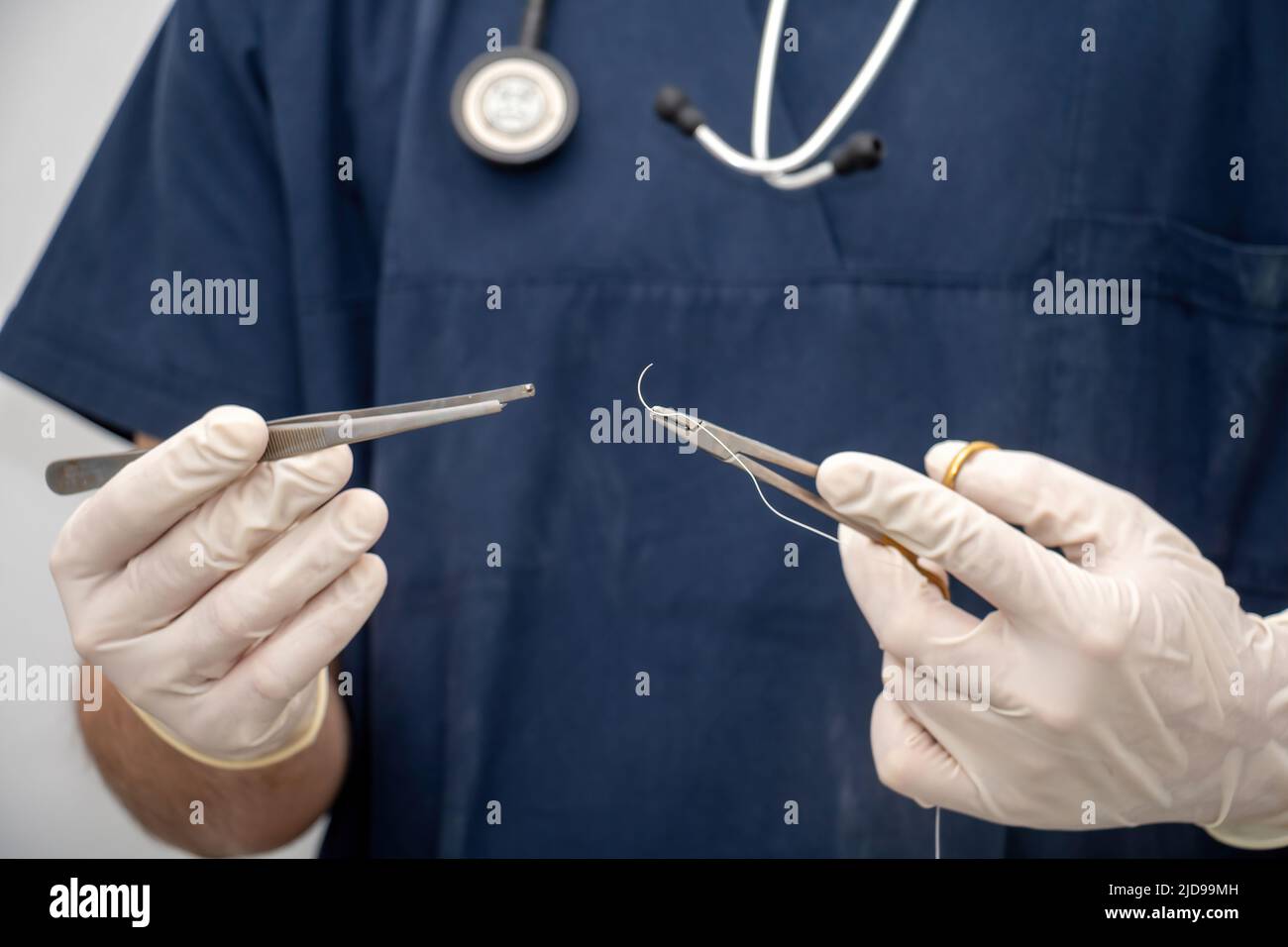 Arzt in medizinischen Uniform hält, in der Hand mit Einweg-Handschuh, chirurgisches Instrument, Zeps und Nadelhalter und Nahtfaden. Arzt verwischen mit Stockfoto