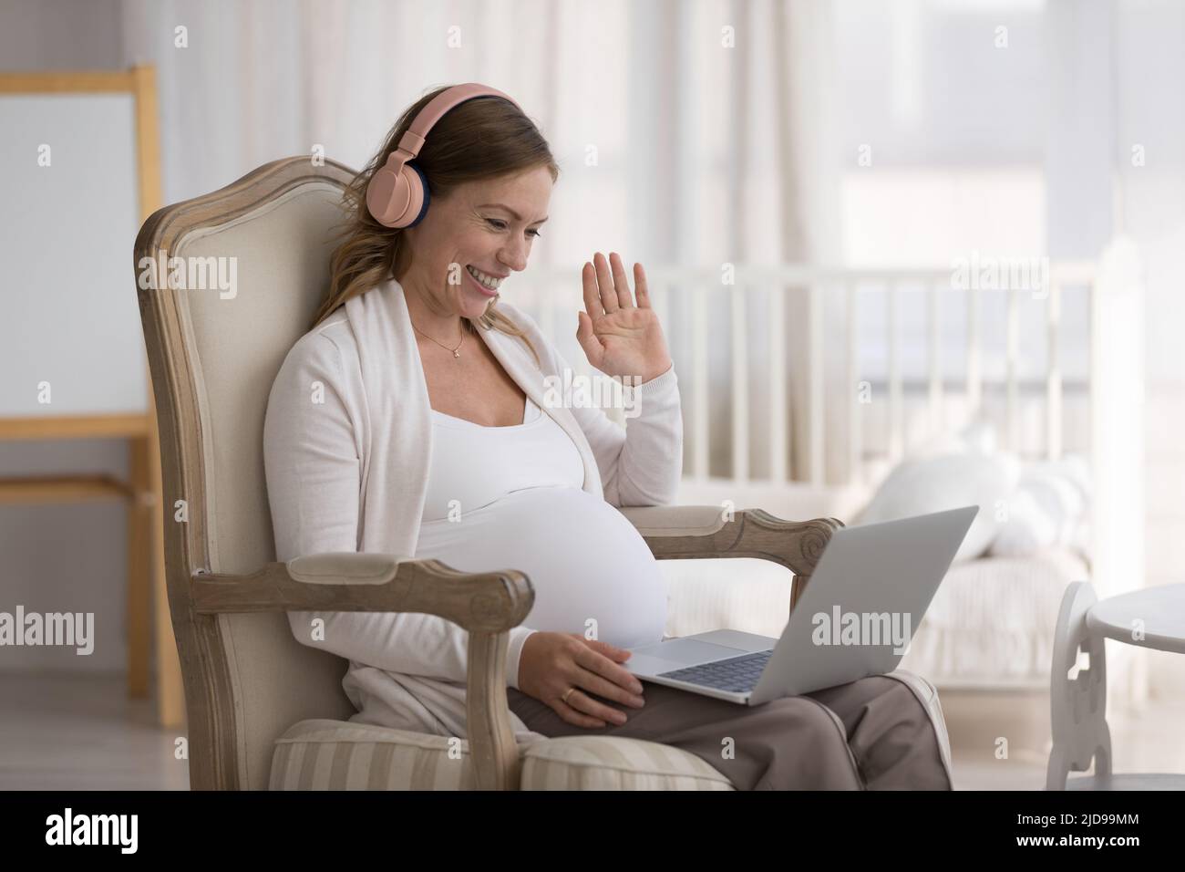 Schwangere starten Videoanruf, sitzend im Sessel mit Laptop Stockfoto