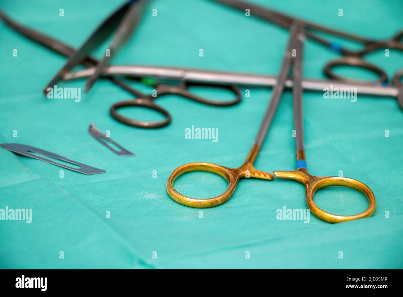 Sterilisiertes Operationsinstrument auf grünem Stoffhintergrund. Chirurg Arzt Edelstahl Werkzeug, Klinge, Nadelhalter oder Treiber, verschwommen Zepern und sciss Stockfoto