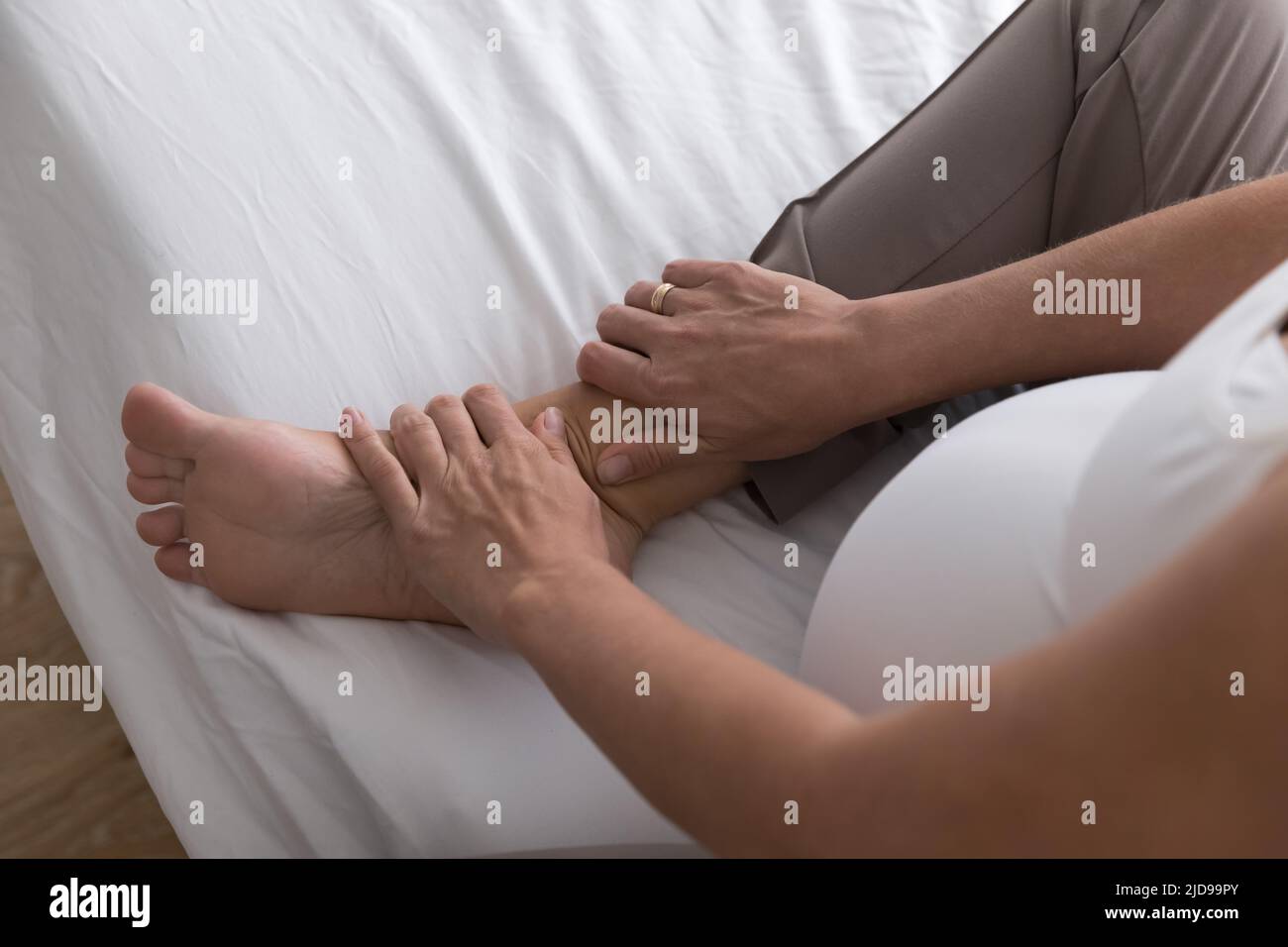 Eine Schwangerin sitzt auf dem Bett und massiert ihren geschwollenen Fuß Stockfoto