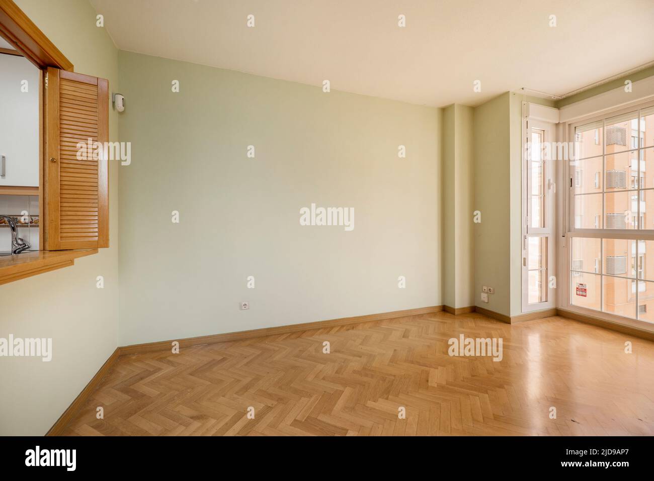 Leeres Wohnzimmer mit Eichenparkettboden mit Erkerfenster auf der einen Seite und Servierluke mit Holztüren im venezianischen Stil auf der anderen Stockfoto