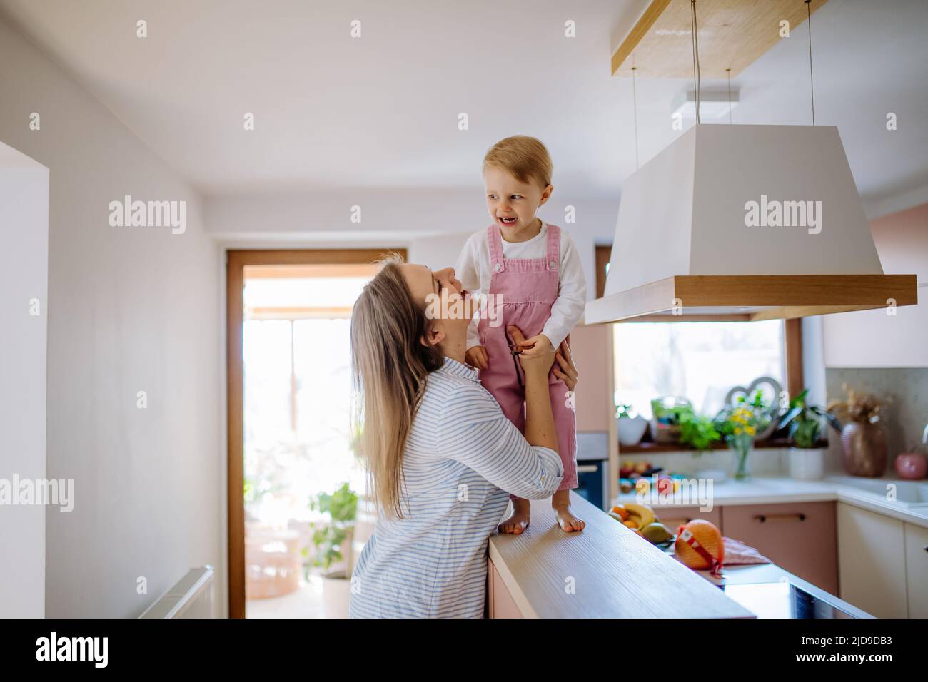 Die junge Mutter hält ihre kleine Tochter, als sie zu Hause auf der Küchentheke läuft. Stockfoto