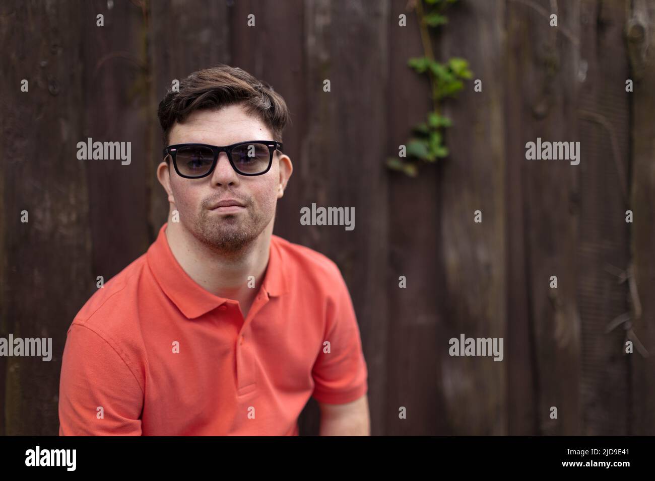 Porträt eines glücklichen jungen Mannes mit Down-Syndrom, der im Park steht und eine Sonnenbrille trägt Stockfoto