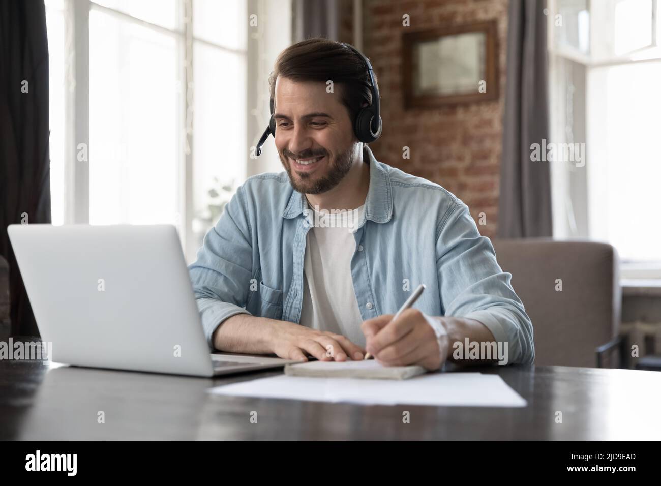 Mann trägt ein Headset und studiert online am Schreibtisch mit einem Laptop Stockfoto