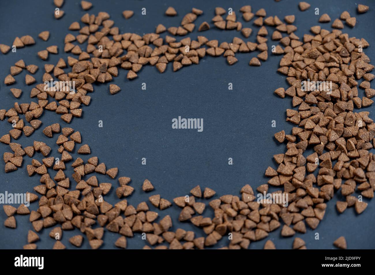 Nahaufnahme von trockenen Katzenfutter-Pellets vor grauem Hintergrund. Braune dreieckige Pellets. Gesundes Futter für Haustiere. Selektiver Fokus. Platz für Text und kopieren Stockfoto