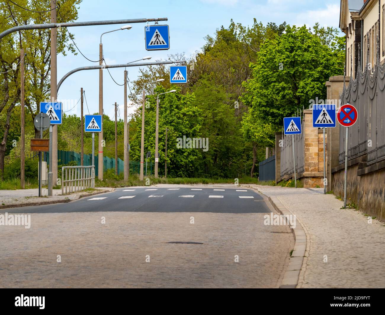 Fußgängerüberweg mit vielen Verkehrsschildern. Viele blaue Schilder neben der Straße, um Autofahrer vorsichtig und vorausschauend zu machen. Stockfoto