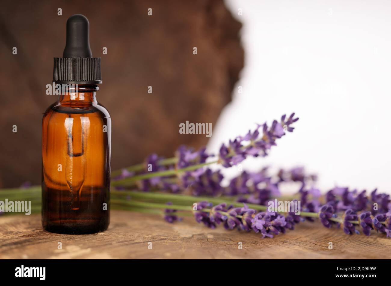 Lavendelöl in Flasche mit Tropf auf Holzstamm. Natürliche Zusammensetzung. Stockfoto