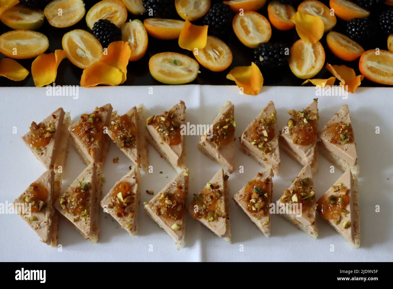 Canapés mit Foie Gras auf Toast mit Moltebeermarmelade und gehackte Nüsse auf Tablett mit Kumquats, Brombeeren und gelben Rosenblättern verziert Stockfoto