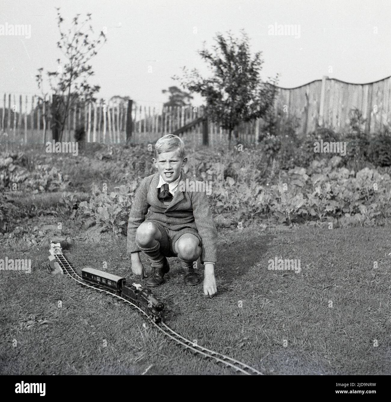 1940s, historisch, ein junger Schuljunge, der sich draußen auf einem Rasen niederkniet, um neben seinem Aufwind-Zug auf einer Strecke auf dem Gras ein Foto zu machen, Bramhall, Stockport, England, Großbritannien. Stockfoto