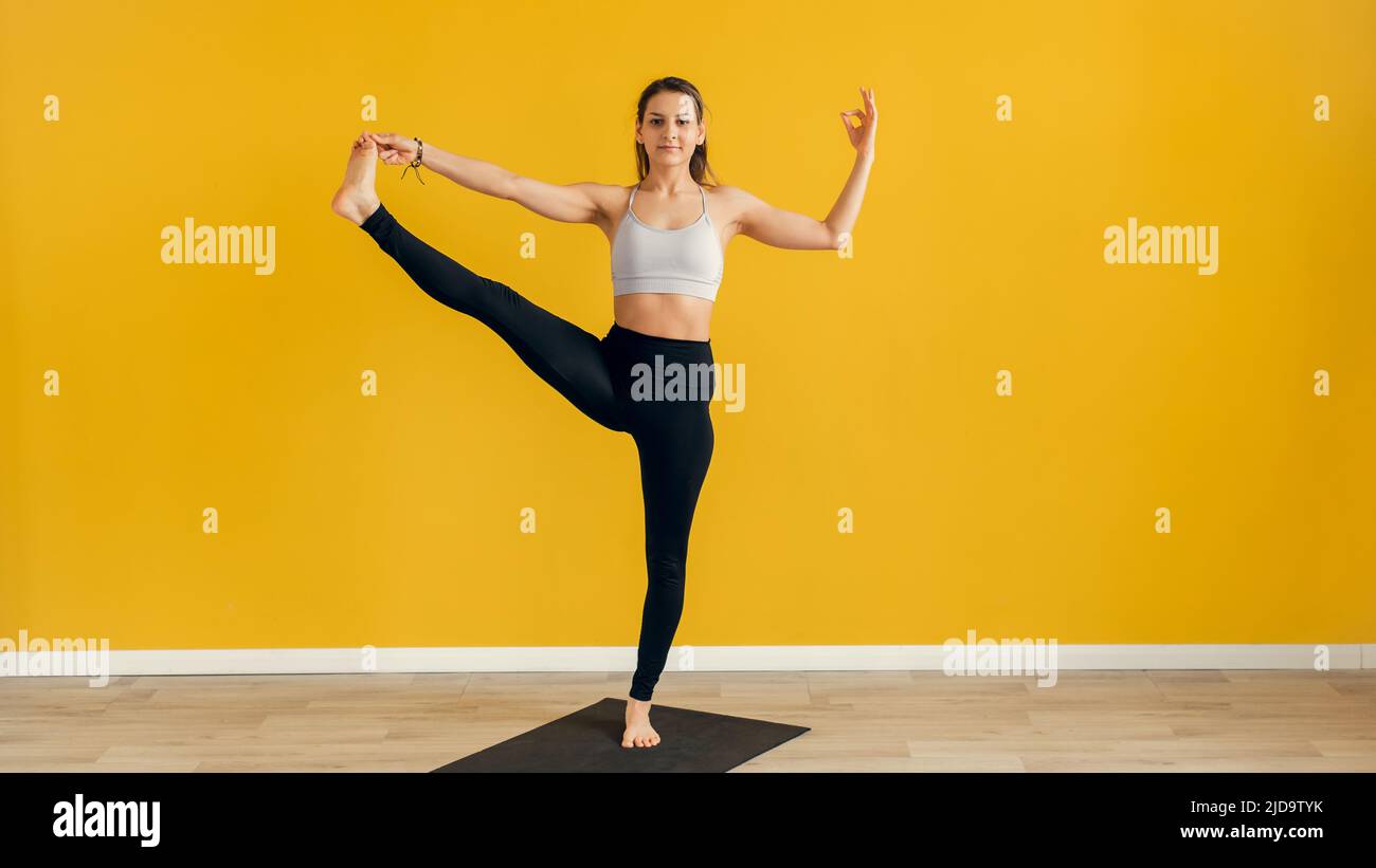 Schöne junge Frau, die drinnen Yoga praktiziert. Utthita Hasta Padangusthasana, von der ausgestreuten Hand bis zur großen Zehe-Pose. Gelber Hintergrund. Webbanner Stockfoto