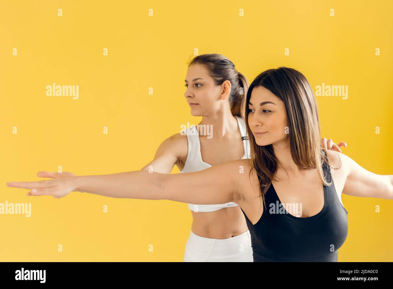 Schöne Frau, die Yoga praktiziert, eine Trainingseinheit mit weiblichen Studenten durchführt, die korrekte Ausführung der Virabhadrasana-Übung zeigt, Krieger Stockfoto