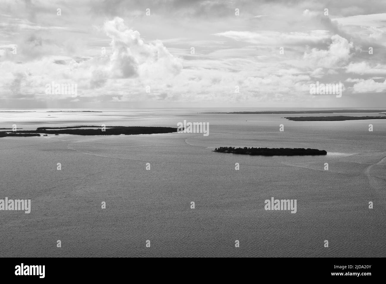 Eine schwarz-weiße Luftlandschaft, die an einem bewölkten Tag aufgenommen wurde. Atolle sind vom Karibischen Meer umgeben und Wolken sind im Hintergrund. Belize. Stockfoto