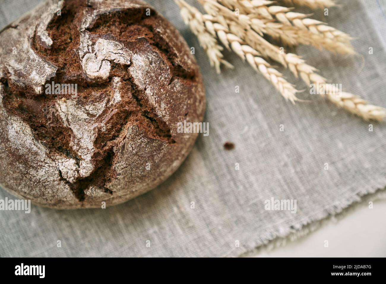 Draufsicht auf frisch gebackenes Roggenbrot auf einer hefefreien Vorspeise und auf einer Mischung aus Vollkorn, Roggen und Weizenmehl. Er liegt auf einer Serviette, neben einer getrockneten Blume mit Körnern. Selektiver Fokus. Stockfoto