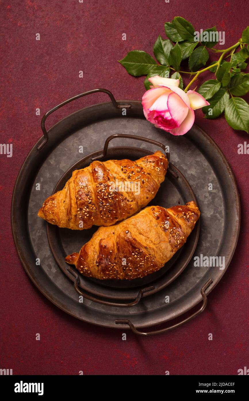 Knusprige, rockige Croissants in einem antiken Metalltablett auf einem burgunderroten Hintergrund, Draufsicht Stockfoto