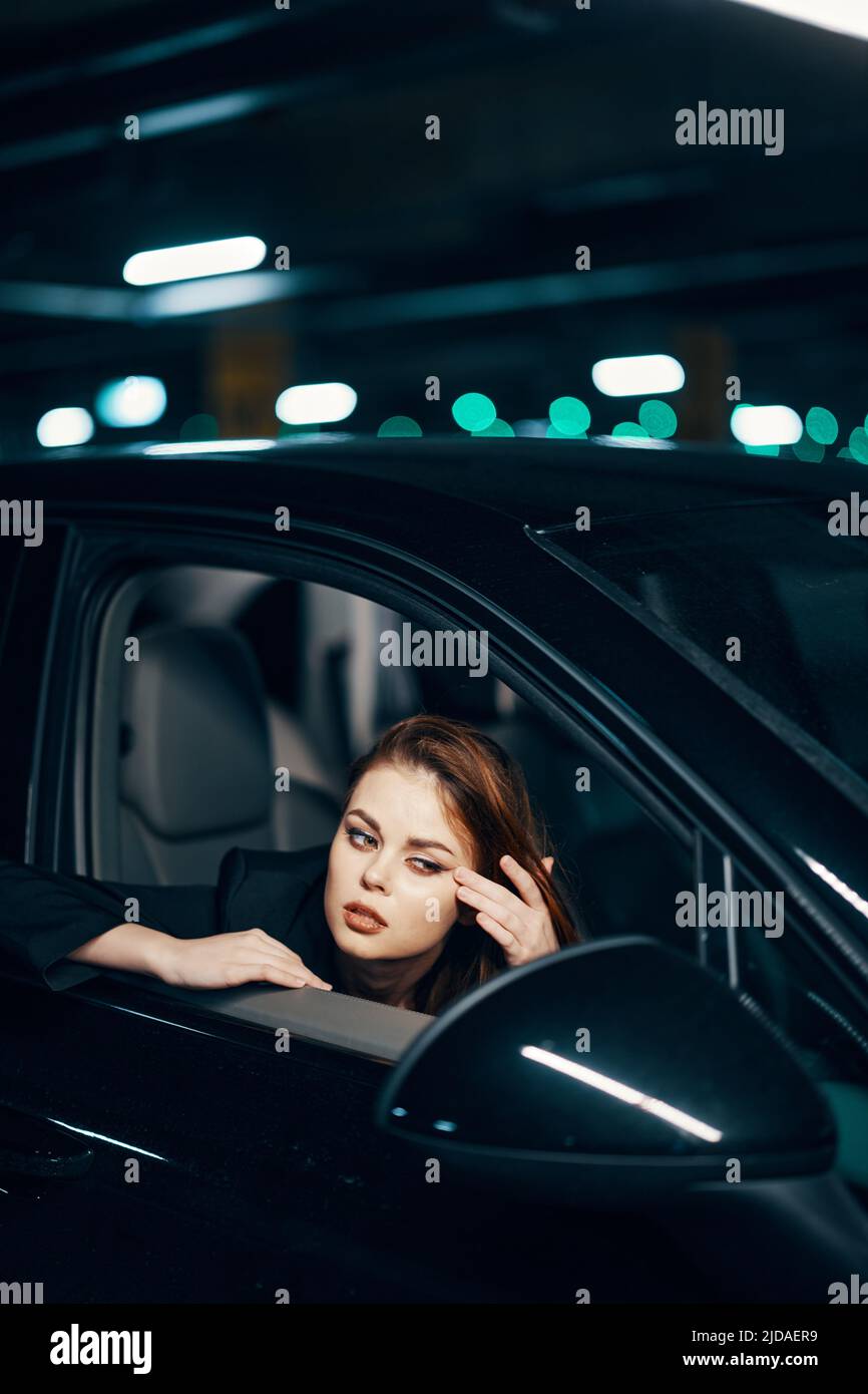 Foto von der Seite, nachts, von einer Frau, die in einem schwarzen Auto sitzt und aus dem Fenster schaut und sanft ihr Gesicht berührt, schaut in die Seitenansicht Stockfoto