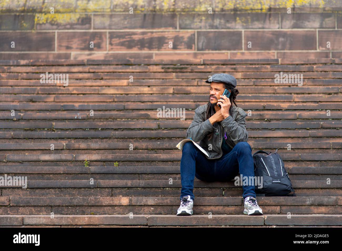 Ein ehrliches Foto eines Mannes, der auf den Stufen der Liverpool Cathedral saß und sich am Telefon unterhielt. England, Großbritannien Stockfoto