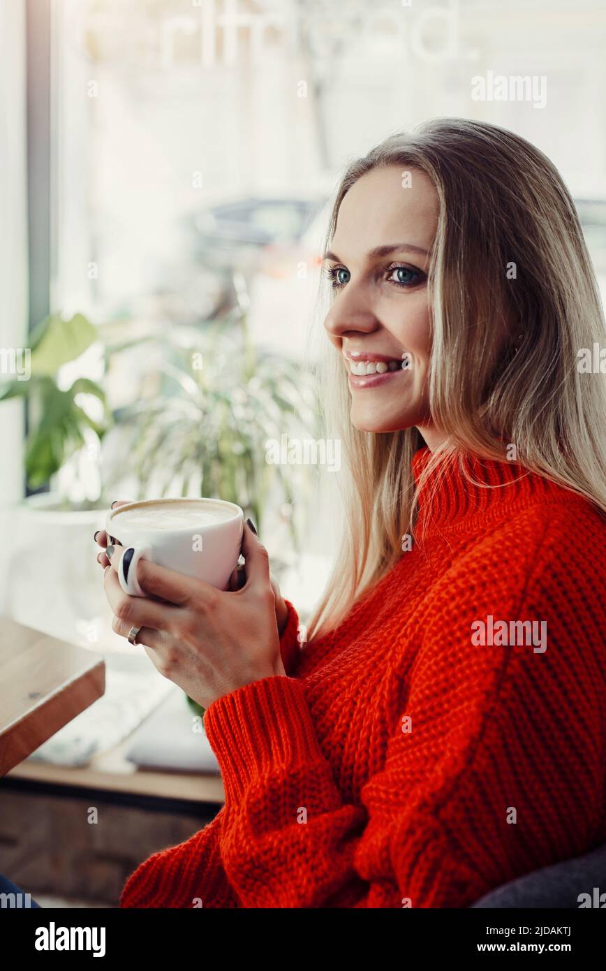 Hübsche junge Frauen trinken heißen Kaffee im Café. Person, die eine Tasse Cappuccino über dem Fenster hält und sich in der Stadt ausruhen kann. Besucher mit kurzer Bremse Stockfoto