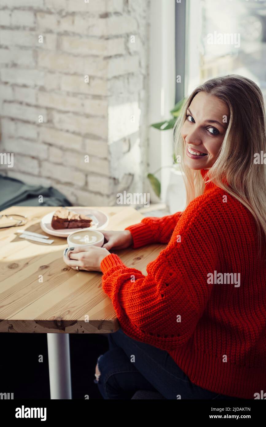 Hübsche junge Frauen trinken heißen Kaffee im Café. Person, die eine Tasse Cappuccino über dem Fenster hält und sich in der Stadt ausruhen kann. Besucher mit kurzer Bremse Stockfoto
