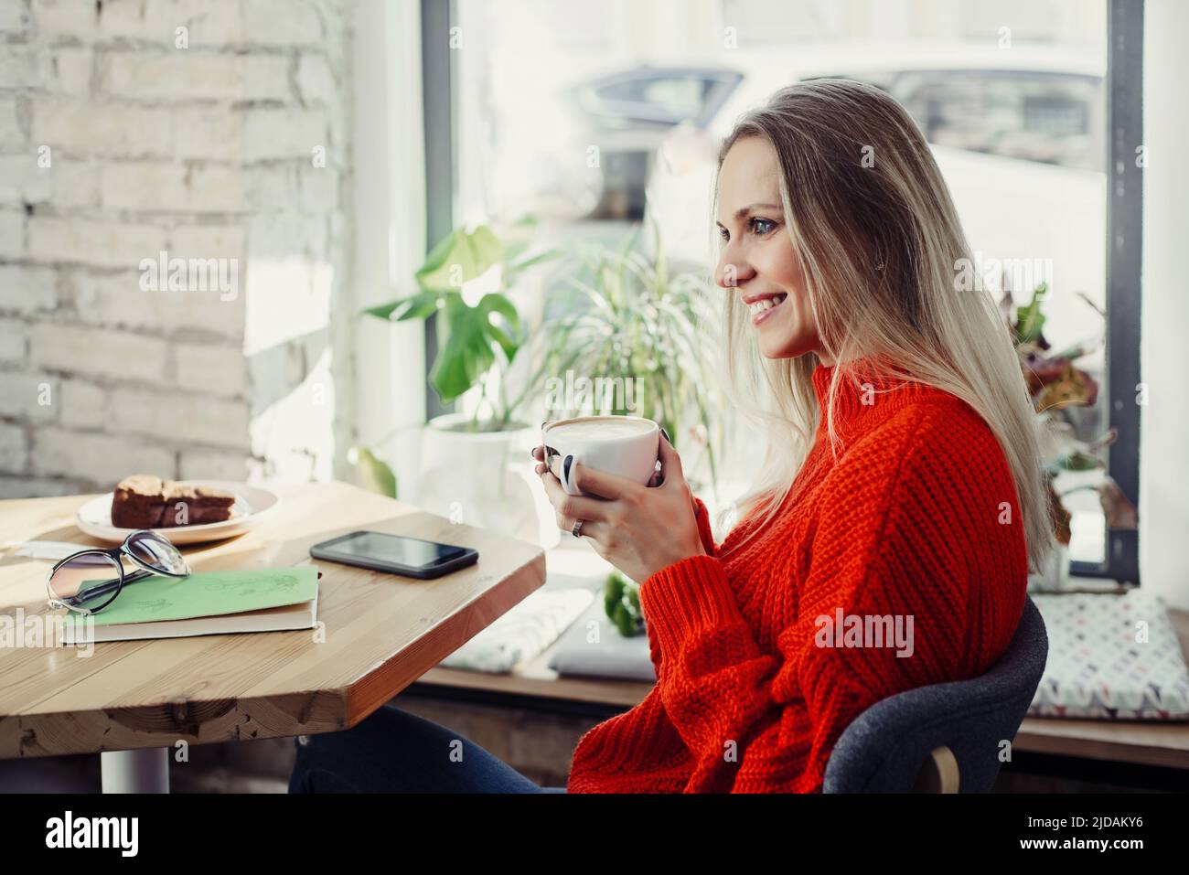 Hübsche junge Frauen trinken heißen Kaffee im Café. Person, die eine Tasse Cappuccino über dem Fenster hält und sich in der Stadt ausruhen kann. Besucher mit kurzer Bremse Stockfoto