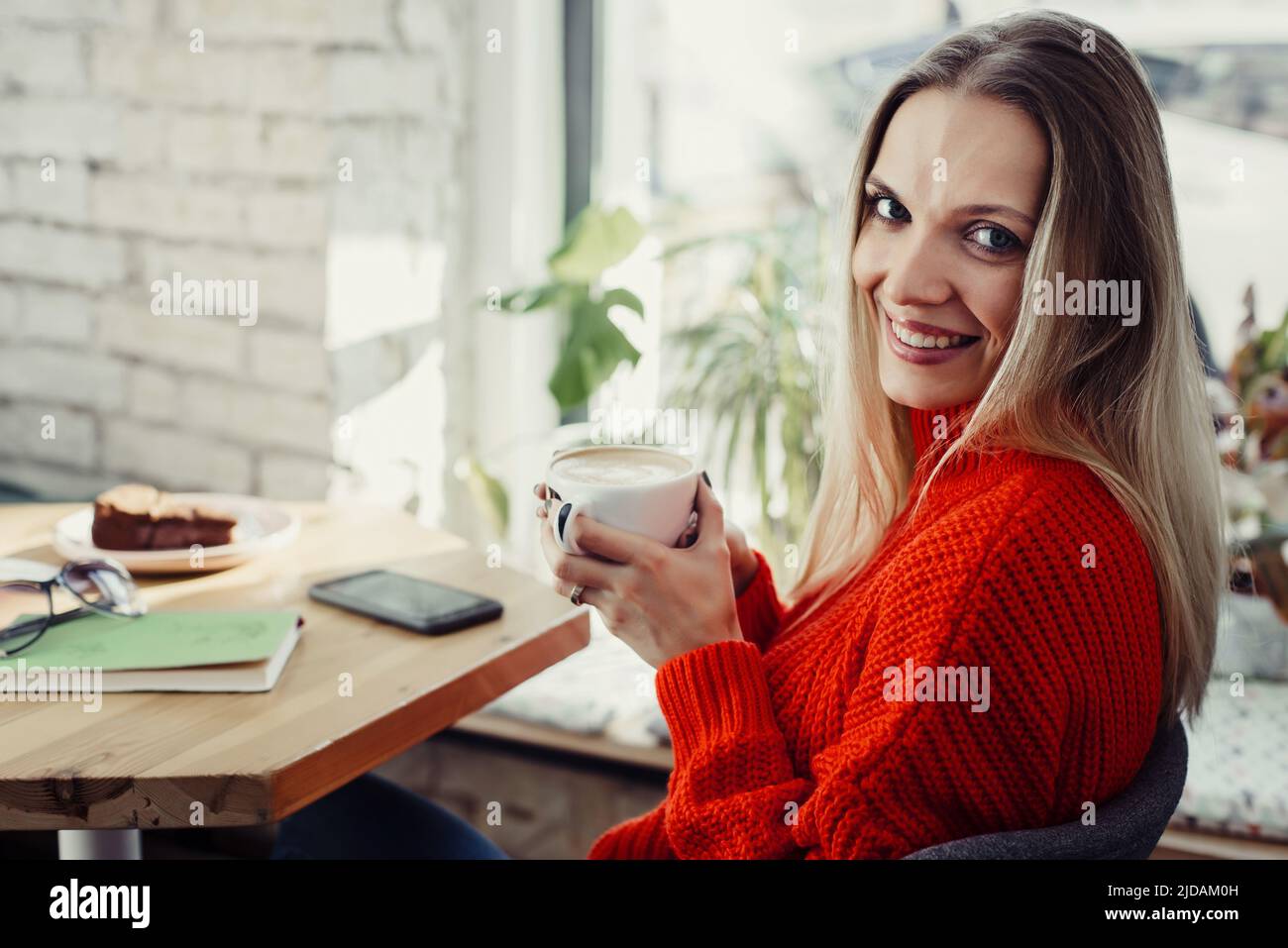 Hübsche junge Frauen trinken heißen Kaffee im Café. Person, die eine Tasse Cappuccino über dem Fenster hält und sich in der Stadt ausruhen kann. Besucher mit kurzer Bremse Stockfoto