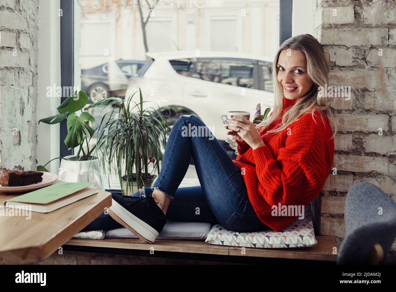 Hübsche junge Frauen trinken heißen Kaffee im Café. Person, die eine Tasse Cappuccino über dem Fenster hält und sich in der Stadt ausruhen kann. Besucher mit kurzer Bremse Stockfoto