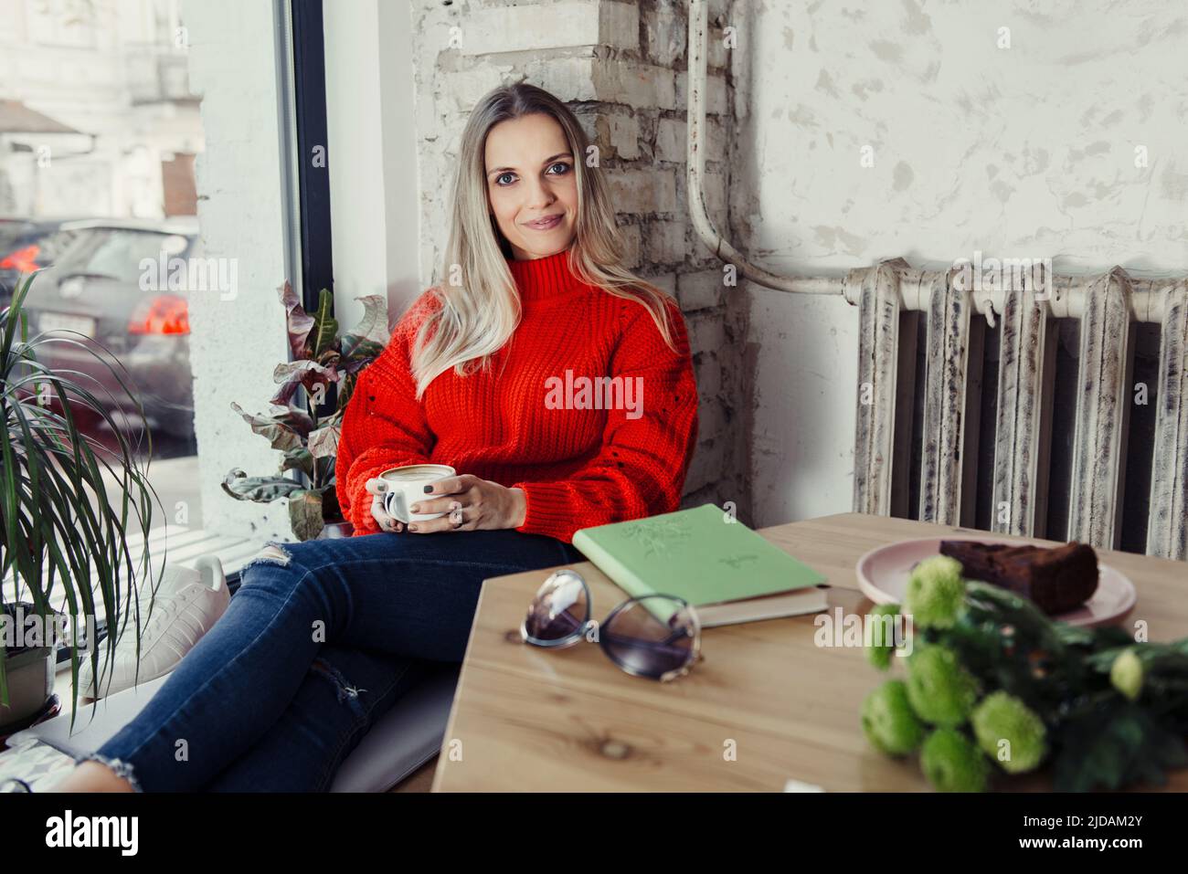 Hübsche junge Frauen trinken heißen Kaffee im Café. Person, die eine Tasse Cappuccino über dem Fenster hält und sich in der Stadt ausruhen kann. Besucher mit kurzer Bremse Stockfoto