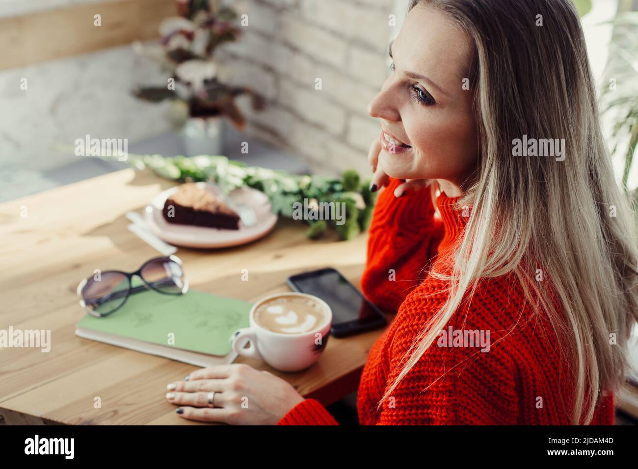Hübsche junge Frauen trinken heißen Kaffee im Café. Person, die eine Tasse Cappuccino über dem Fenster hält und sich in der Stadt ausruhen kann. Besucher mit kurzer Bremse Stockfoto