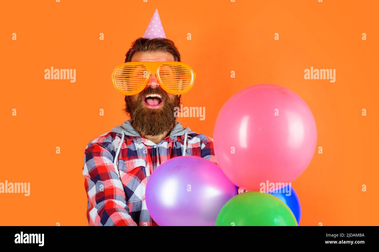 Bärtiger Kerl in lustigen Gläsern und Kegelhut mit Ballons. Mann auf der Party. Alles gute zum Geburtstag. Stockfoto