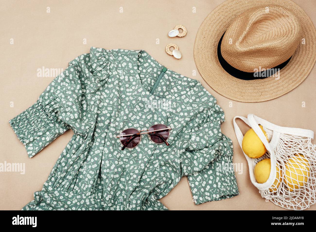 Sommerlicher Casual-Style. Stilvolle Frauenkleidung und Accessoires. Kleid, Sonnenbrille, Hut und Zitronenfrüchte in Netztasche auf beigem Hintergrund. Flach liegend, top vie Stockfoto