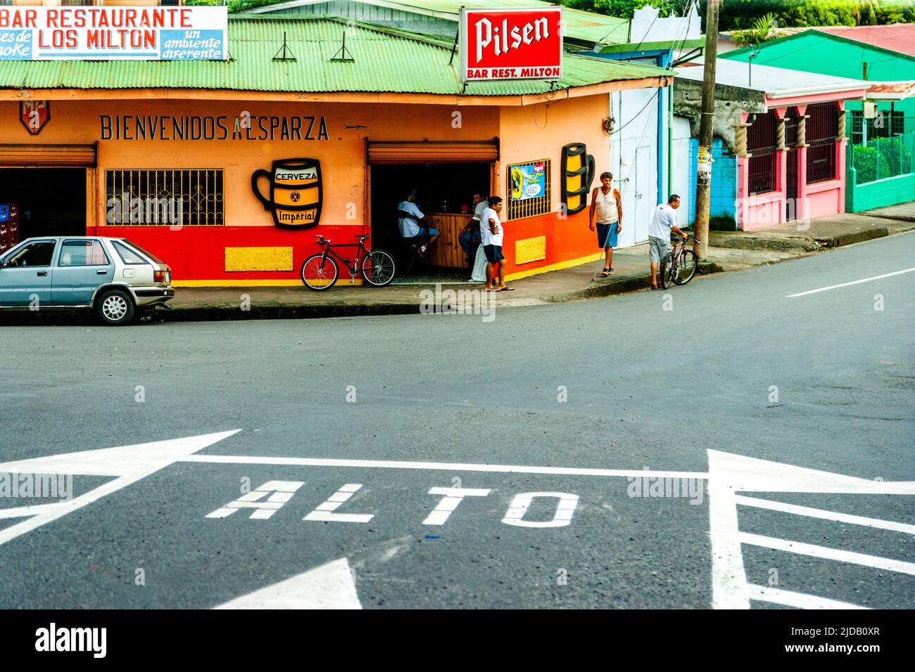 Costa Rica Kreuzung mit einer Bar auf der anderen Straßenseite, wo eine Gruppe von Männern Bier trinken. Stockfoto