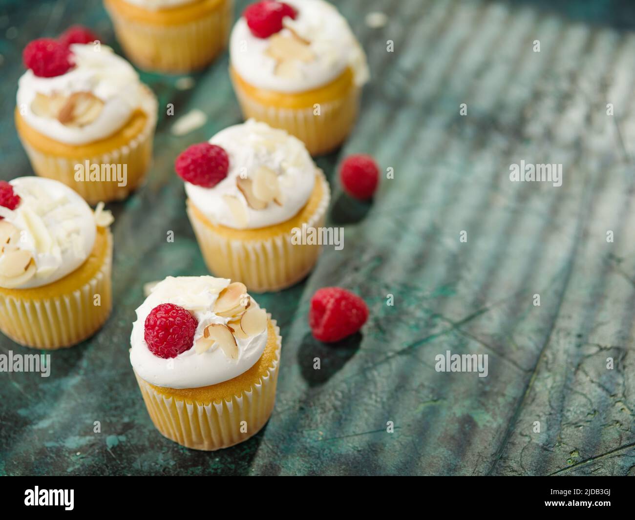 Leichte, frische Muffins mit Creme, verziert mit Himbeeren und Mandeln auf einer grünen Serviette. Hintergrund der Speisen. Food Design, Süßes Essen, Urlaub, Geburtstag, Stockfoto