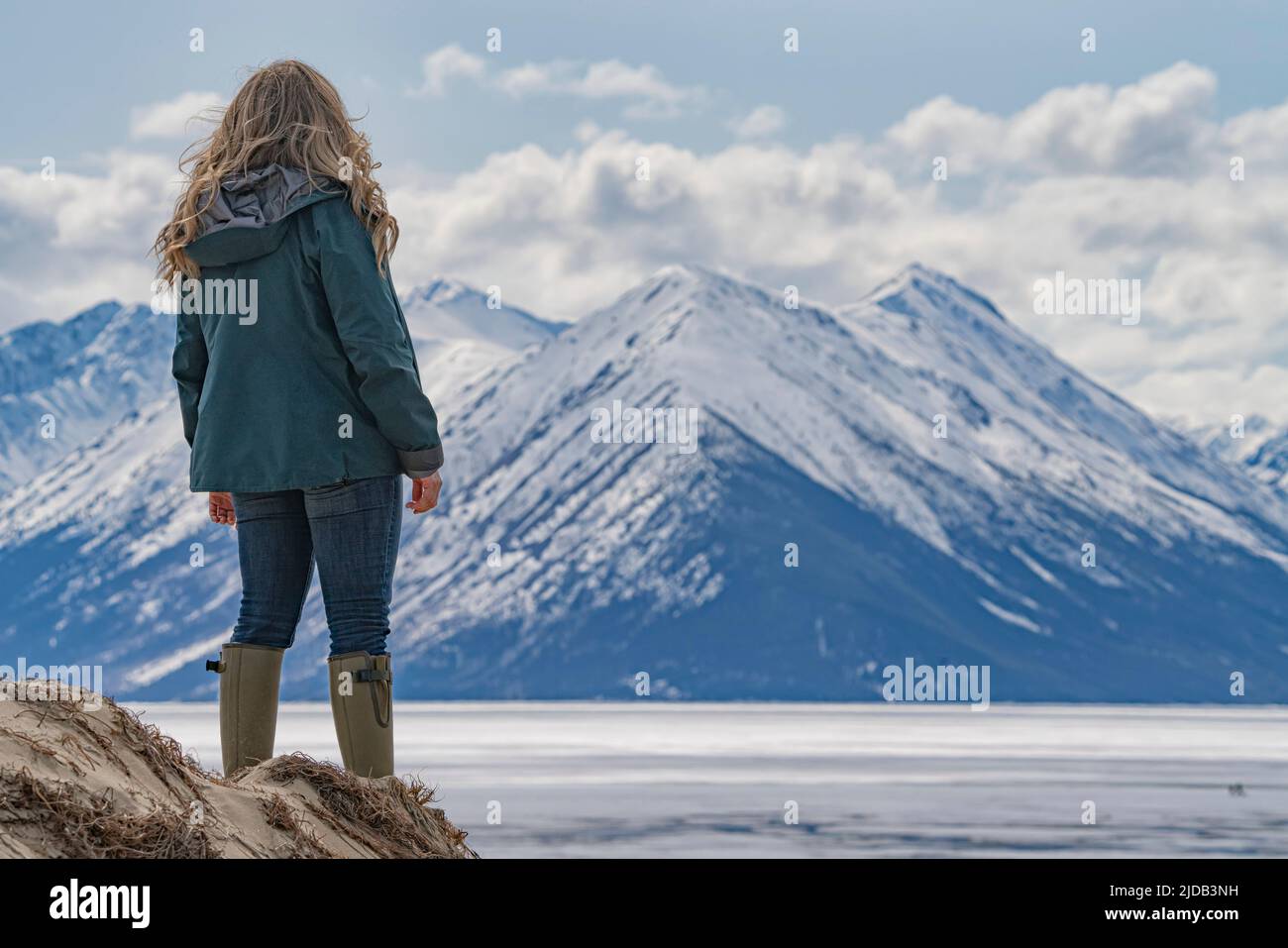 Blick von hinten auf eine Frau, die auf den Sanddünen steht und auf den gefrorenen Bennett Lake und die schneebedeckten Berge um Car blickt... Stockfoto