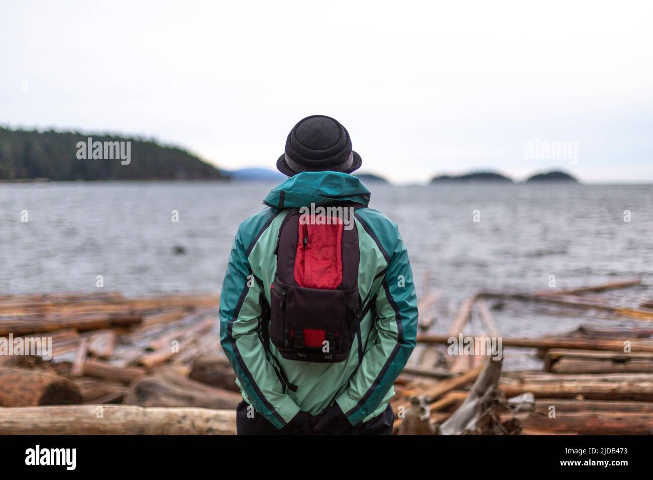 Person mit Hut und Rucksack steht mit Blick auf den Ozean und die Küste, Sunshine Coast, BC, Kanada; British Columbia, Kanada Stockfoto