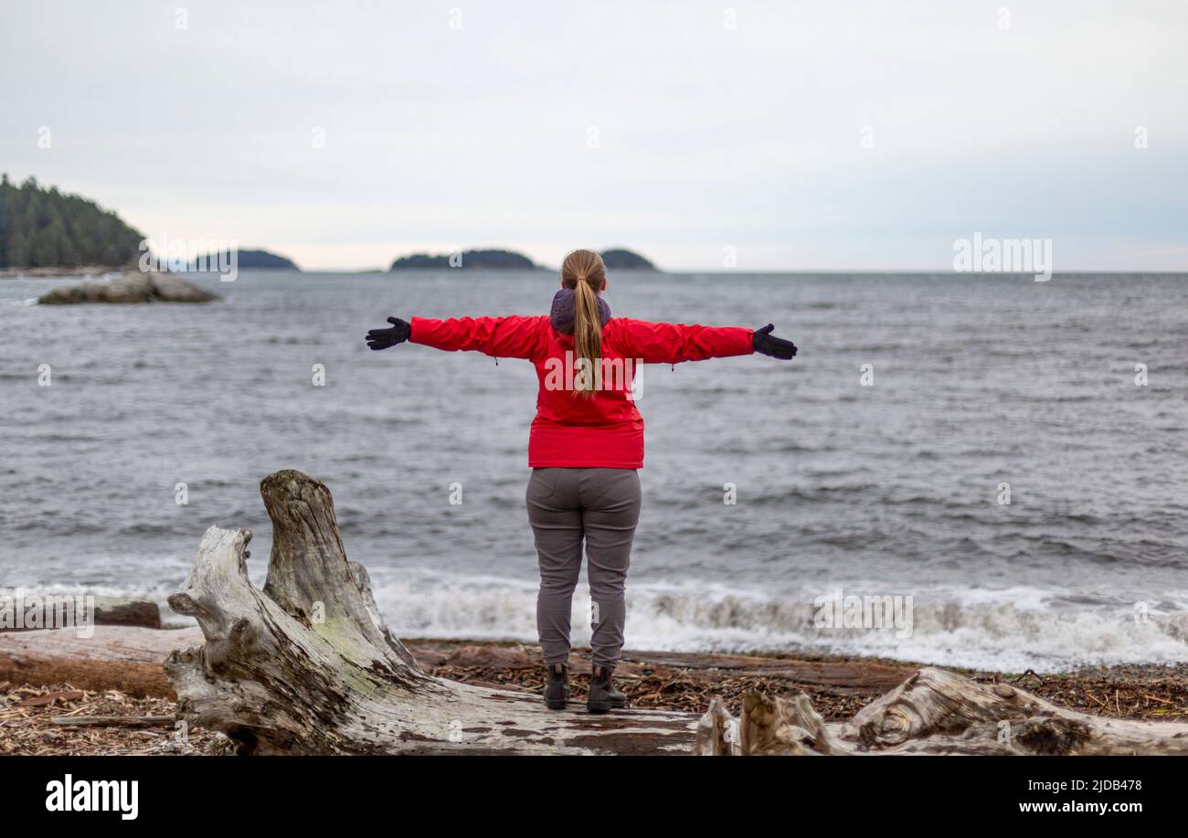 Frau steht am Ufer und blickt mit ausgebreiteten Armen auf das Meer, Sergeant Bay, Sunshine Coast; British Columbia, Kanada Stockfoto
