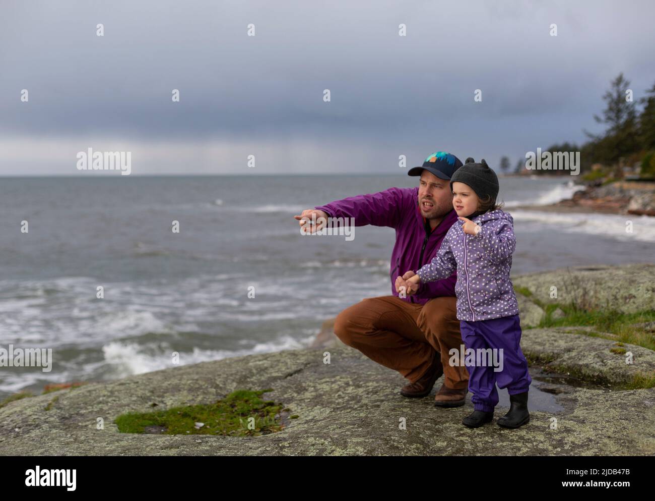 Vater hält die Hand seiner kleinen Tochter, während sie am Wasser stehen und auf das raue Meer blicken, Sunshine Coast, BC, Ca... Stockfoto