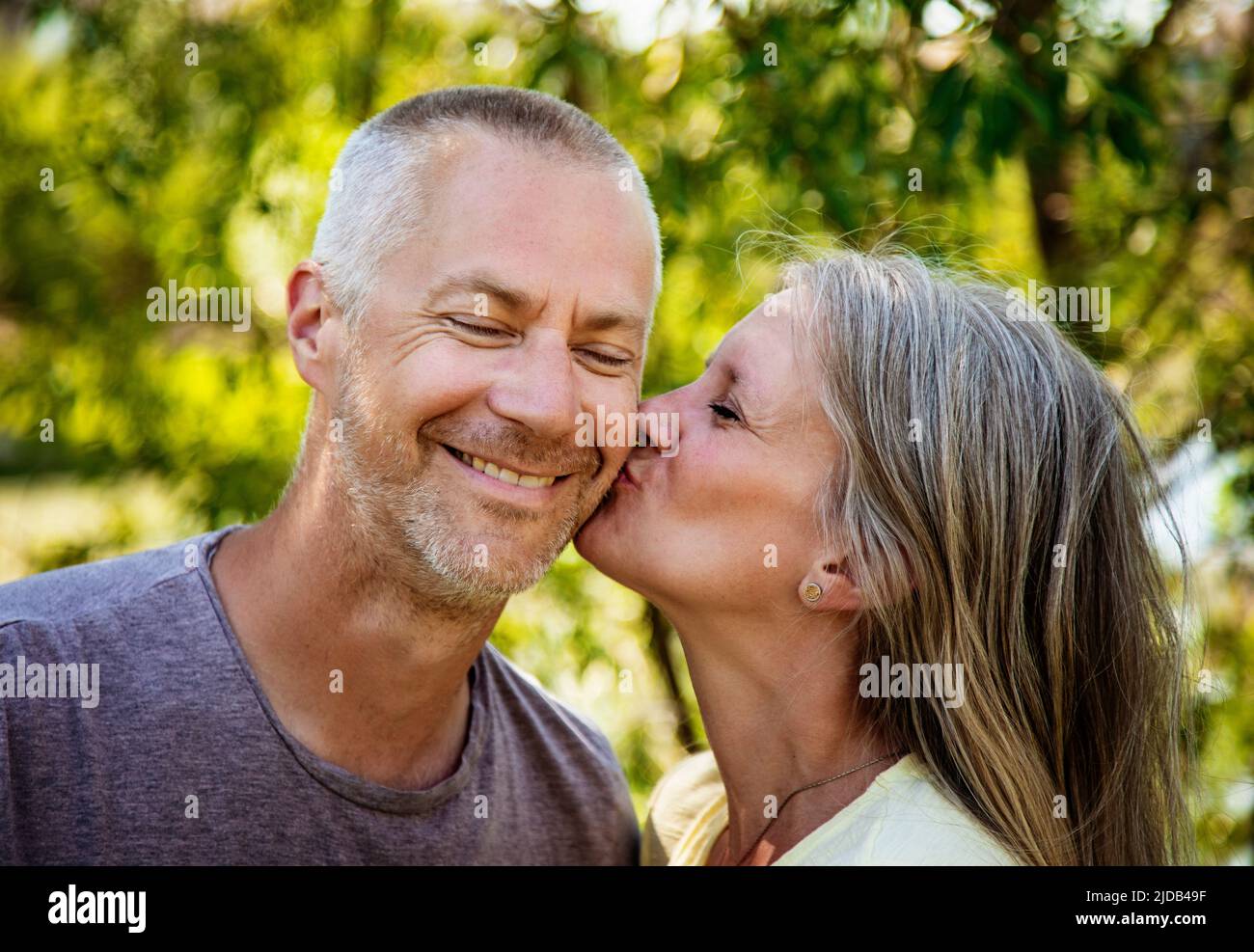 Porträt eines erwachsenen Ehepaars, das draußen mit einer Frau zusammen ist, die ihrem Mann die Wange küsst; Edmonton, Alberta, Kanada Stockfoto