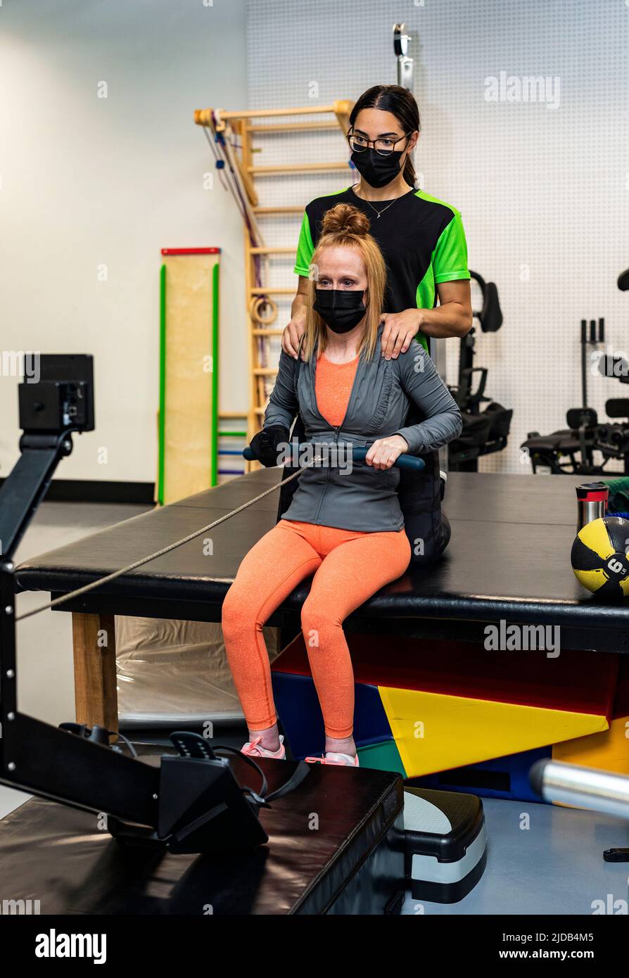 Eine querschnittsgelähmte Frau, die mit ihrem Trainer an einem Rudergerät trainiert; Edmonton, Alberta, Kanada Stockfoto