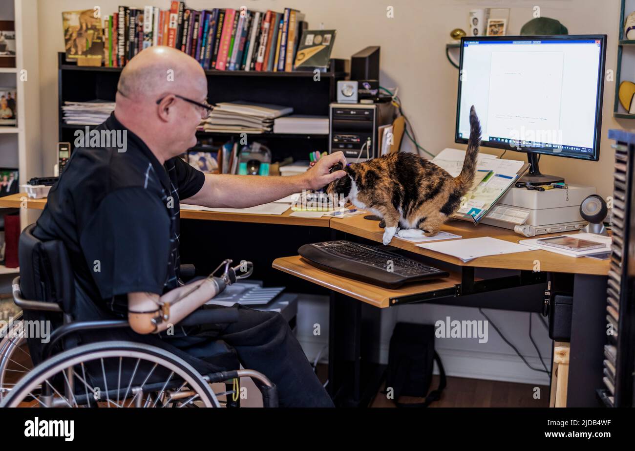 Ein Mann mit einer Amputation von zwei Gliedmaßen, der von zu Hause aus an einem Computer arbeitet Albert, Alberta, Kanada Stockfoto