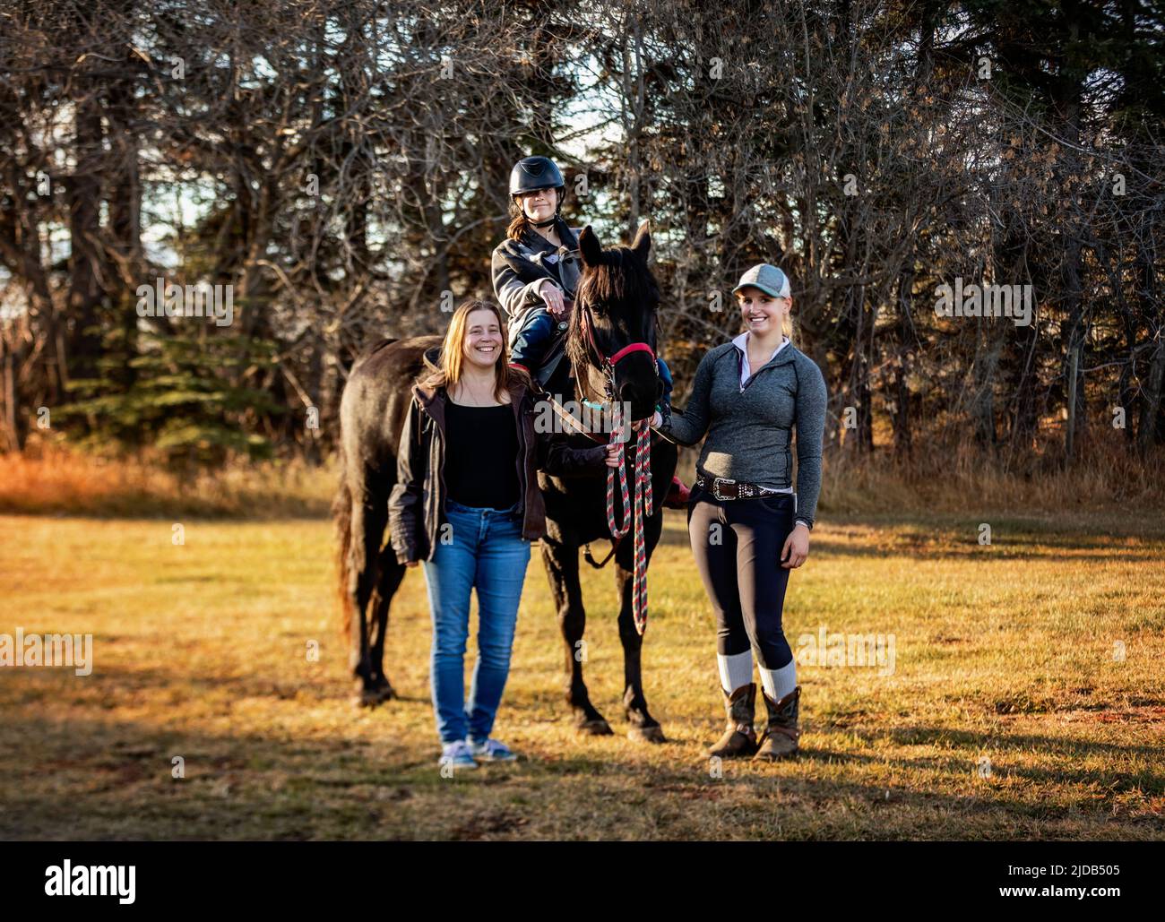 Ein junges Mädchen mit Zerebralparese posiert mit ihrer Mutter, ihrem Trainer und einem Pferd während einer Hippotherapie-Sitzung nach einem Trail-Ritt Stockfoto