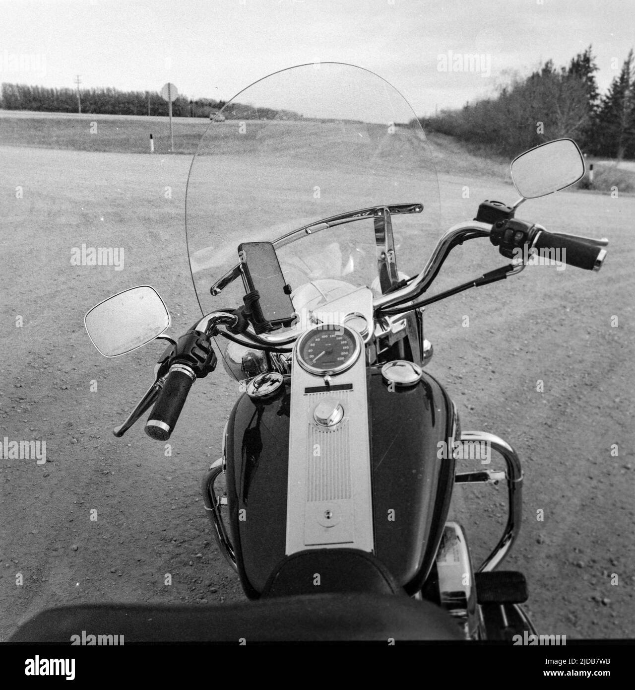 Ansicht des Lenkers, des Armaturenbretts und der Windschutzscheibe eines Motorrads, das an einer Straßenabzweigung geparkt ist, mit einem Smartphone in einer Halterung; Manitoba, Kanada Stockfoto