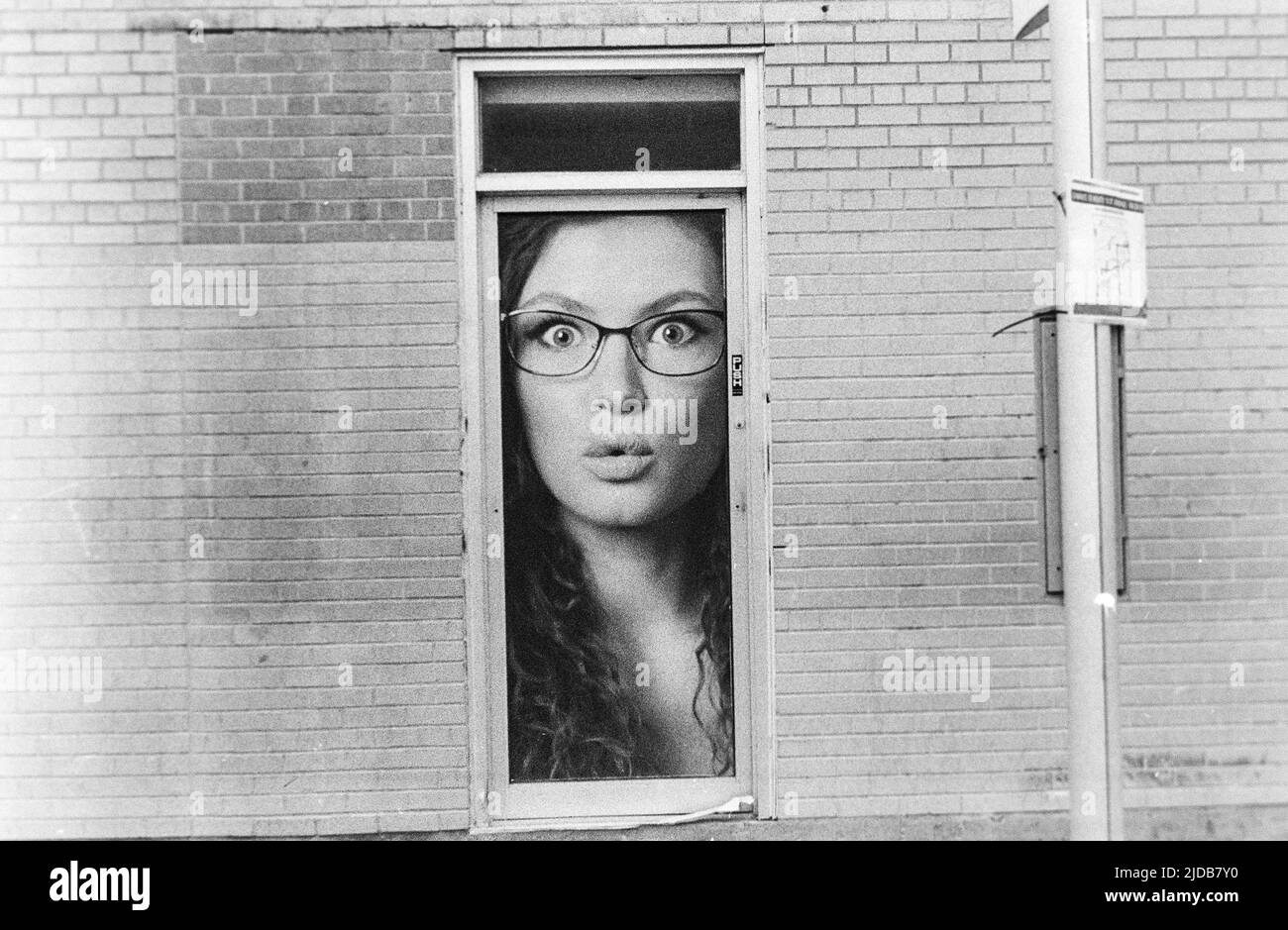 Das Gesicht einer Frau, die aus einem kleinen Fenster eines Ziegelgebäudes schaut; Winnipeg, Manitoba, Kanada Stockfoto