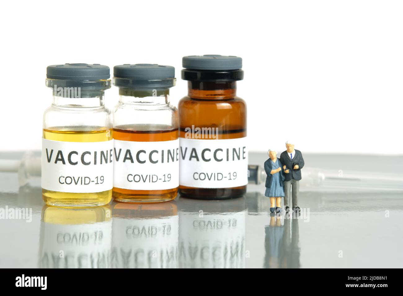 Miniatur Menschen Spielzeug konzeptuelle Fotografie. Ein älteres Paar, das vor einer Impfampulle steht. Gesundheitsmedizinisches Konzept. Isoliert auf weißem Hintergrund Stockfoto