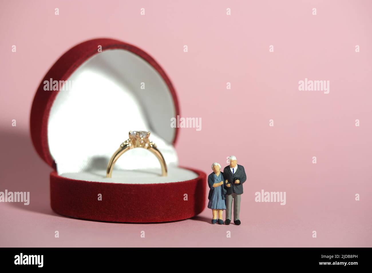 Miniatur Menschen Spielzeug konzeptuelle Fotografie. Ein älteres Paar, das vor dem roten Herzringkasten steht. Konzept für Hochzeit, Hochzeitstag. Bild pho Stockfoto